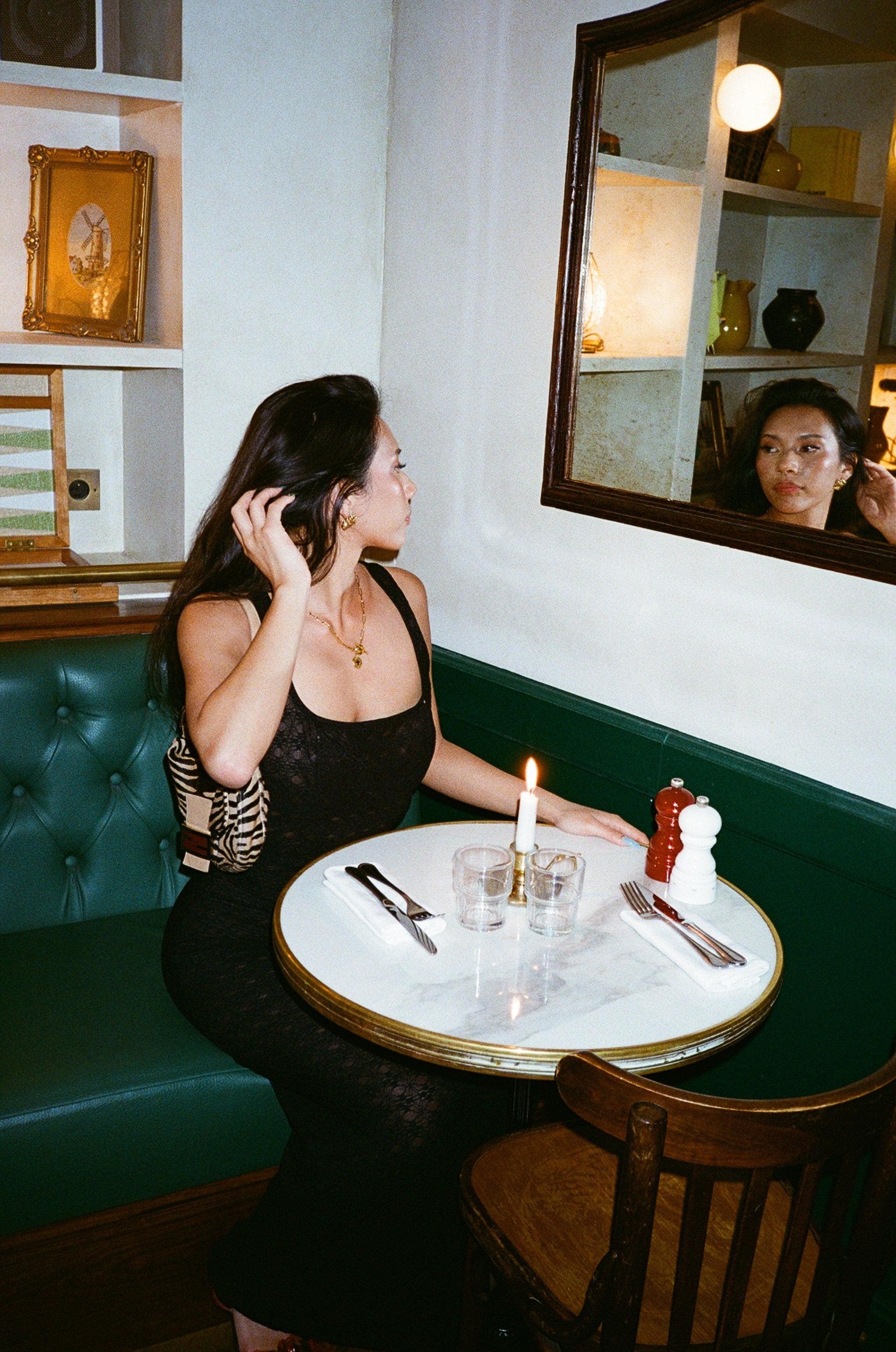 a woman in a lace dress sat at a table in a restaurant looking in the mirror 